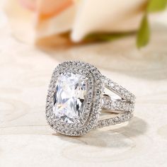 an engagement ring with a large cushion cut diamond surrounded by smaller round diamonds on a white background