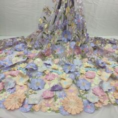 a table topped with lots of flowers covered in sheers and lace on top of a white sheet