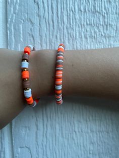 two bracelets with orange and white beads on someone's arm