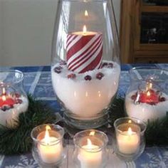 a table topped with lots of candles next to a glass vase filled with snow and candy canes