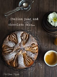 a cake with icing and powdered sugar on it next to two cups of coffee