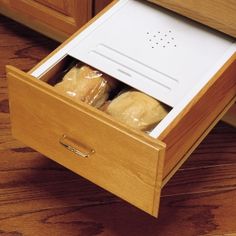 an open drawer with bread in it on the floor next to a wooden counter top