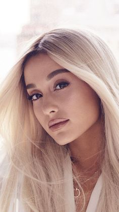 a woman with long blonde hair wearing a white shirt and looking off to the side