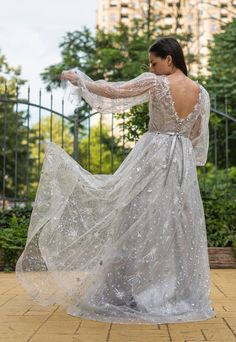 a woman in a long white dress is standing on a brick walkway with her arms outstretched