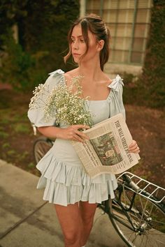 a woman is walking down the street with flowers in her hand while holding a newspaper