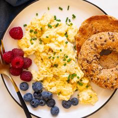 a breakfast plate with bagel, scrambled eggs and berries on it next to a fork