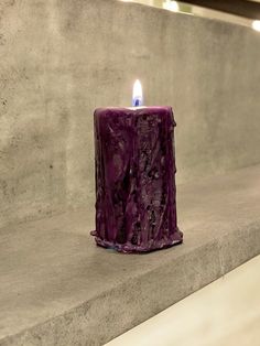 a purple candle sitting on top of a cement wall next to a light blue flame