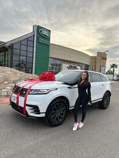 a woman standing next to a white car with a red ribbon on it