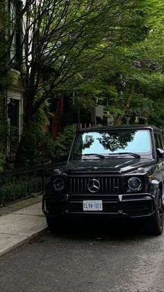 a black car parked on the side of a road next to a tree filled street