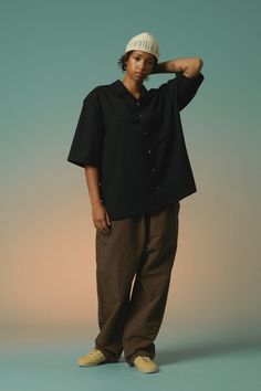 a man standing in front of a green background wearing a black shirt and brown pants