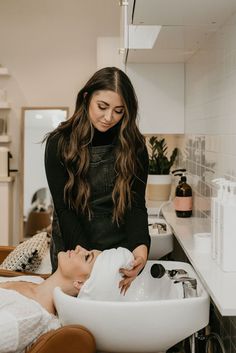 a woman is getting her hair washed in the sink while another woman looks on from behind