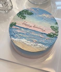 a round cake decorated with palm trees and the words happy birthday on it, sitting on top of a table