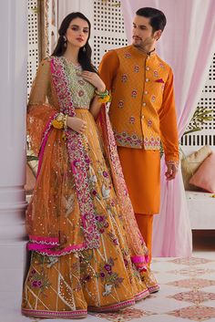 a man and woman standing next to each other wearing orange outfits with pink flowers on them