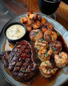 steak, shrimp and scallops on a plate next to a glass of wine