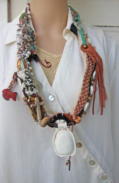 This large lightweight fabric and leather necklace is new, handmade, and one of a kind.  It slips easily over the head and is 34" around, made of different fabrics and textiles, suede and leathers.  I beaded this necklace with beads made of wood, bone, shells, cowry shells, brass, glass, plastic, and faux pearls. I added a black bow charm, a silver charm with a branch impression, a flying dove, and a painted vintage Mexican fish charm. There is also a small wooden cross, woven beaded leather, and a white leather fob that I made after looking at rustic African Akan jewelry from about 1950. This necklace is photographed being worn by a lifesize mannequin, and also next to a ruler. It is new and was made in a smoke-free environment. It has a very eclectic Bohemian feel, and looks elegant when White Leather Bohemian Jewelry, White Bohemian Leather Jewelry, Bohemian White Leather Jewelry, Bohemian Leather Necklace For Festivals, Handmade Bohemian Leather Necklace, Mexican Fish, Flying Dove, Leather Fob, Textile Necklace