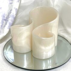 two white glass vases sitting on top of a silver plate next to each other