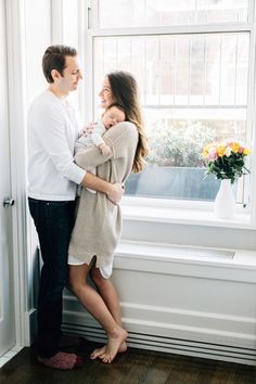 a man and woman standing next to each other in front of a window with flowers