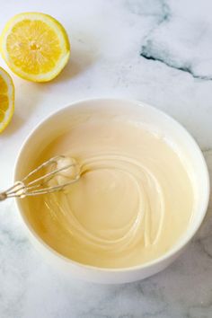 a white bowl filled with liquid next to sliced lemons on a marble counter top