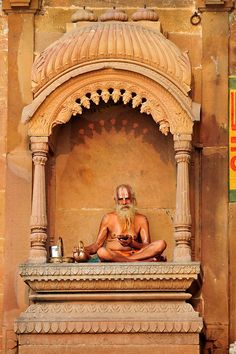 a man sitting on top of a stone bench in front of a building next to a cup