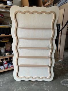 an unfinished wooden frame sitting on the floor in a room filled with shelves and tools