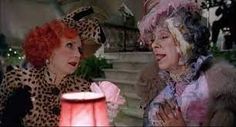 two women dressed in costume talking to each other while standing next to a pink light