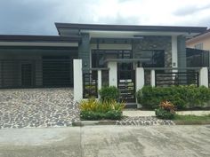 a house that is sitting in the middle of a driveway with rocks and plants around it