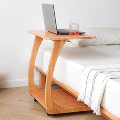 a laptop computer sitting on top of a wooden table next to a bed with white sheets