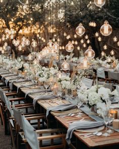 a long table with many lights hanging from the ceiling and flowers in vases on it