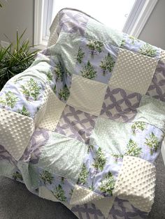 a quilted blanket sitting on the floor next to a potted plant in front of a window