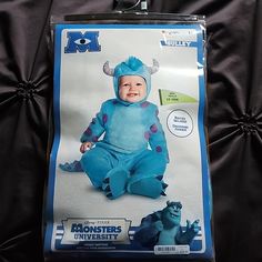 a baby in a blue monster costume sitting on a black surface with the packaging behind it