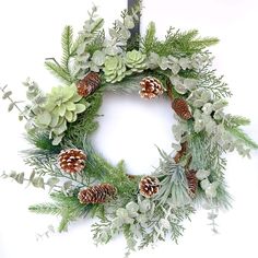 a green wreath with pine cones and greenery