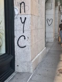 a woman walking down a sidewalk next to a tall building with graffiti on it's side