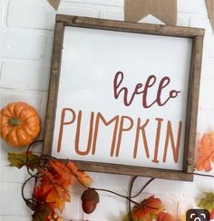 a sign that says hello pumpkin hanging on a brick wall with fall leaves and acorns