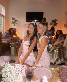 two girls in pink dresses standing next to each other at a table with plates and cups on it