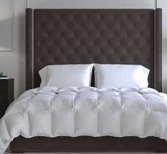 a bed with white sheets and pillows on top of it next to a night stand