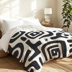 a bed with black and white comforter on top of it in a bedroom next to a potted plant