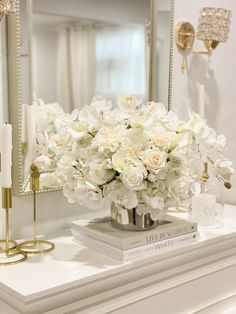 a white flower arrangement sitting on top of a table next to a mirror and candles