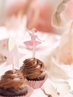 two cupcakes with chocolate frosting and a fairy figurine on top