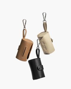 three leather cups hanging from hooks on a white background, one is black and one is tan