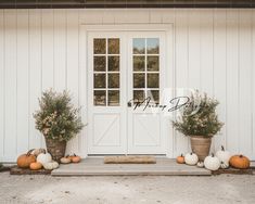 pumpkins and gourds line the front steps of a white house with two large doors