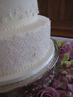 a three layer white wedding cake with purple flowers on the table next to each other