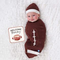 a baby in a football outfit laying next to a sign that says welcome baby on it