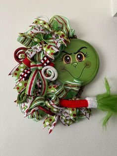 a green christmas wreath with a grin face on it's front door hanger