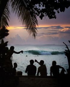 some people are sitting on the beach watching a wave come in to shore and one person is holding his arm out