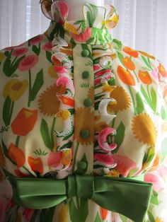 "Here's a lovely 1960's dress, that will just brighten your day, in colorful large flowers, pleated curly collar, sleeve ends and front of the green buttoned bodice. The flowers are in colors of gold, tangerine/orange, pink, and yellow with green grass, leaves, and stems. The long sleeves are a little puffy, with the waistline surrounded with a 2 1/2\" satin bow belt, and a nylon zipper back closure. Dress appears to be never worn, and has no label, a yellow acetate lining. The outer floral fabr Spring Vintage Dress With Covered Buttons, Spring Mod Dresses With Buttons, Retro Green Dress With Buttons, Retro Buttoned Dresses For Garden Party, Retro Dresses With Buttons For Garden Party, Vintage Multicolor Buttoned Dresses, Vintage Multicolor Dresses With Buttons, Bow Belt, Spring Floral Dress