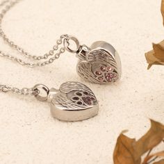 two silver heart shaped pendants sitting on top of a white table next to leaves