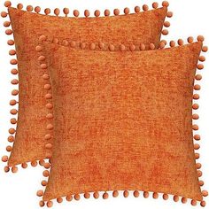 two orange pillows with pom - poms on the front and back of them