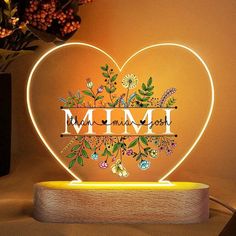 a heart shaped lamp with the word mimi on it and flowers in front of it