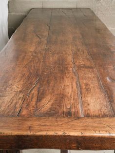 an old wooden table with metal legs in a room that has white walls and concrete flooring