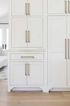 a white kitchen with gold handles and cabinets in the background is a living room area